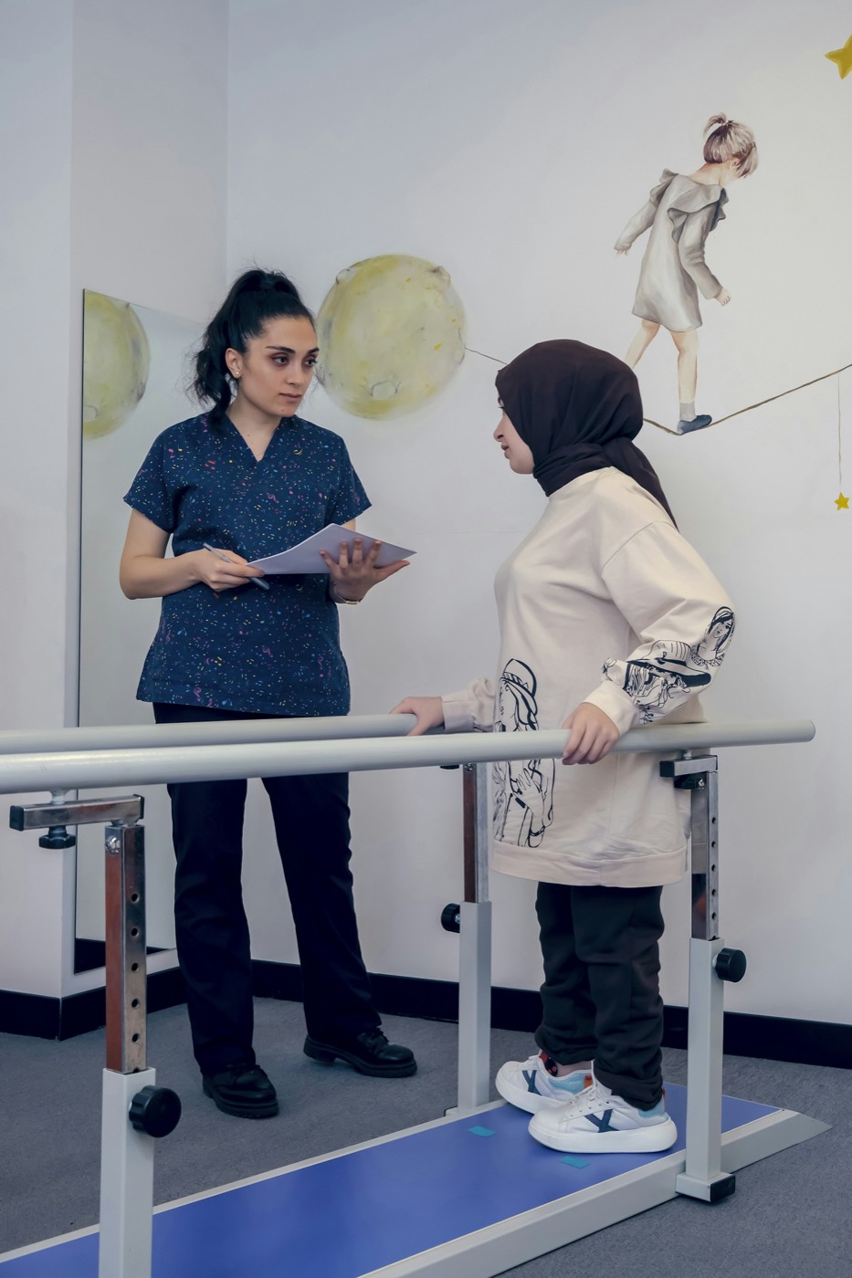 A therapist guiding a woman between parallel bars