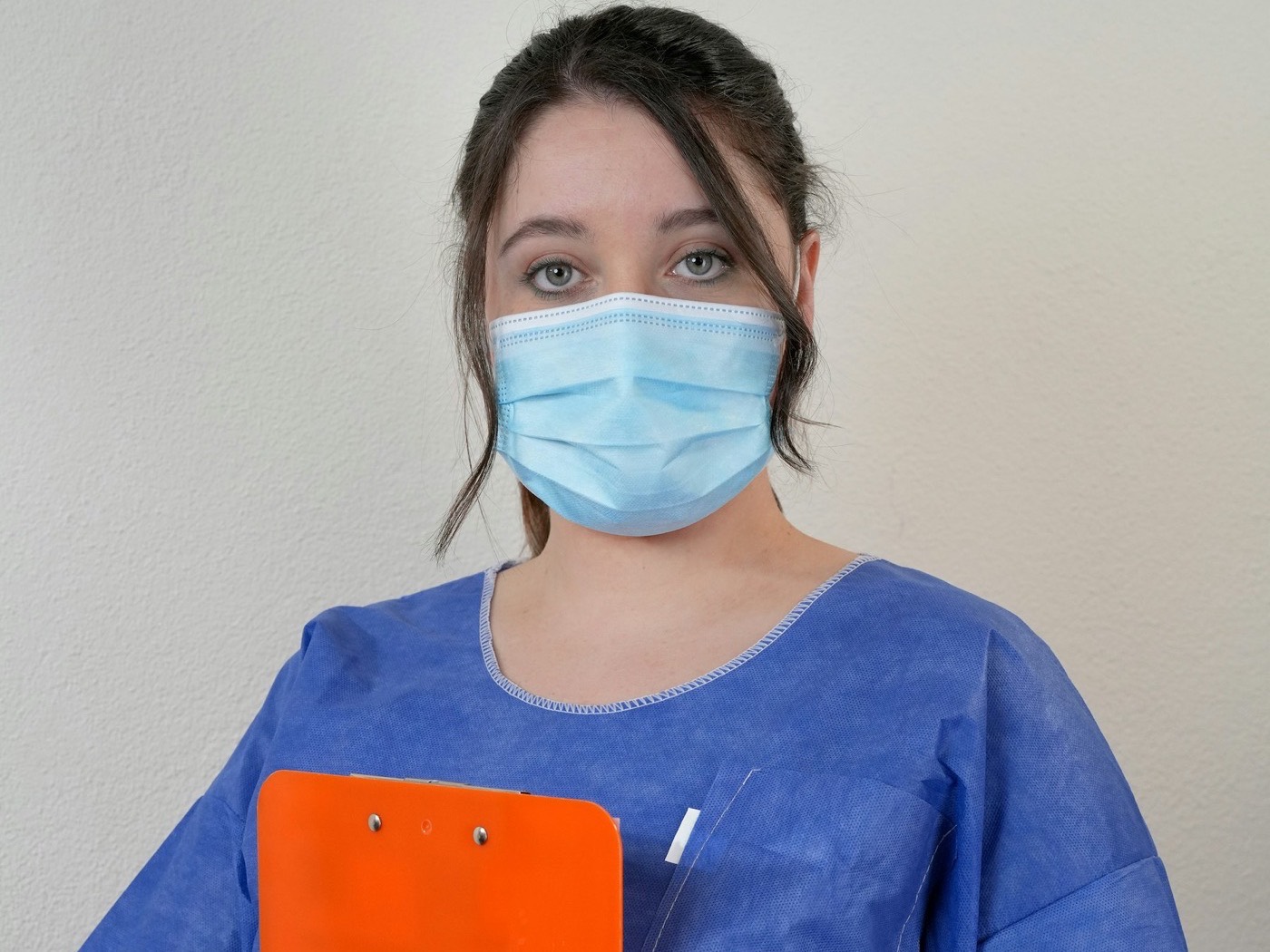 A nurse in blue scrubs holding an orange clipboard